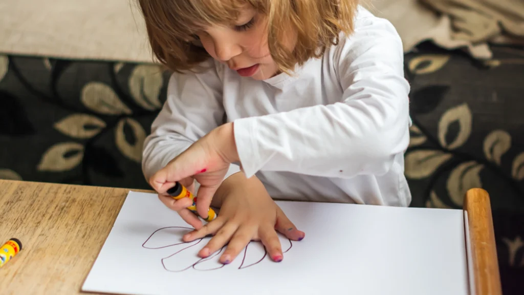 Child tracing around one hand on paper, using one hand to stabilize and the other to draw.