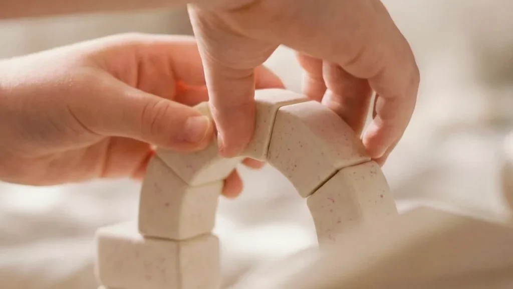 A child uses both hands to connect small curved building pieces, practicing hand coordination and careful placement.